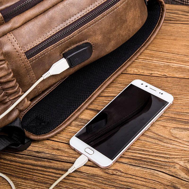 Mochila de cuero compacta para hombre con puerto USB y celular, sobre mesa de madera.