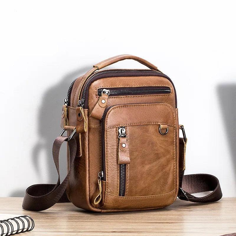 Bolso masculino urbano de piel genuina color marrón con cierres metálicos sobre mesa de madera.