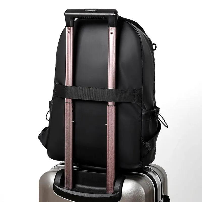 Parte trasera de mochila masculina negra acolchonada sobre maleta de viaje plateada.