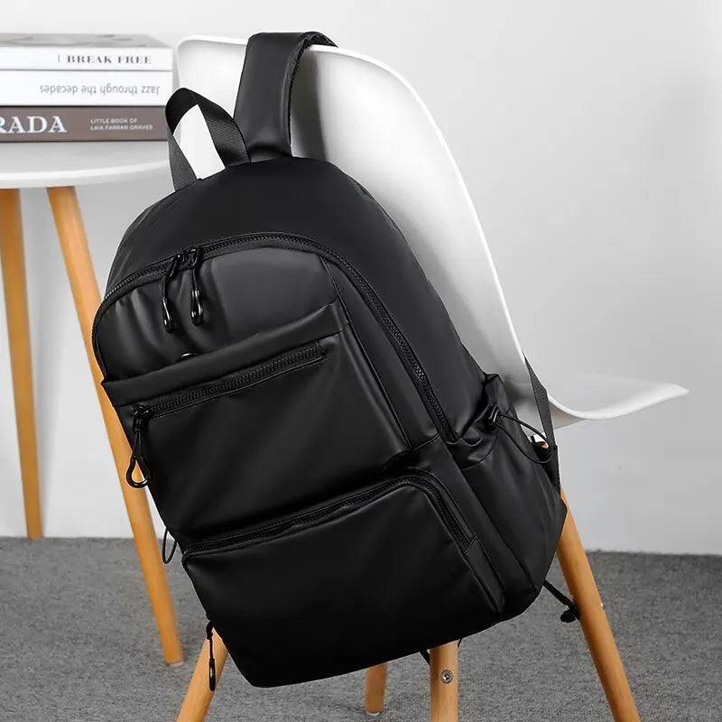 Mochila impermeable negra para hombre, diseño urbano moderno, apoyada en silla blanca