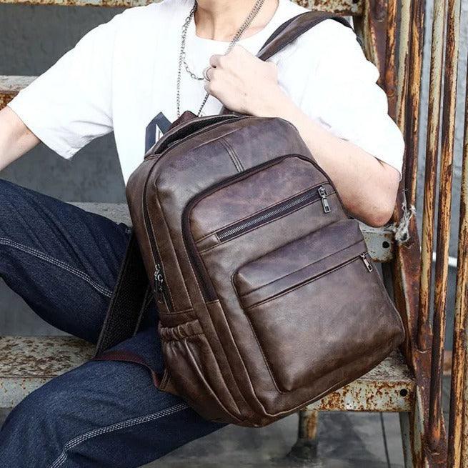 Mochila masculina de cuero marrón estilo urbano, compacta, con múltiples bolsillos frontales.