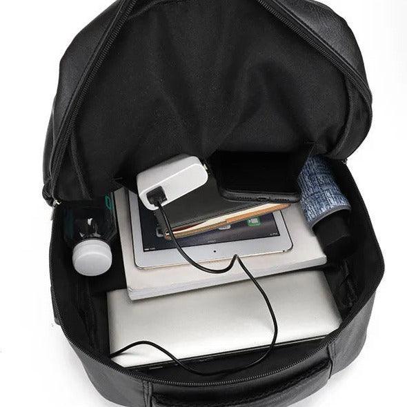 Mochila de cuero negra para hombre, abierta y llena de objetos como laptop y tablet.